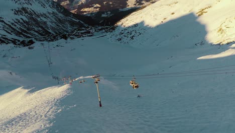 Ski-resort-chairlift-gondola-on-steep-mountain-ski-slopes,-sunset-aerial-view