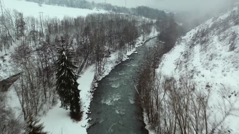 River-flowing-down-snowy-misty-mountainside-valley,-aerial-dolly-view