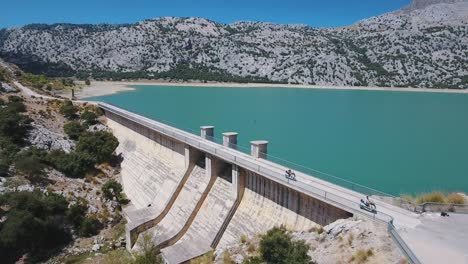 Aerial-footage-in-4k-of-two-scooter-drivers-driving-over-a-freshwater-dam-in-Mallorca---Tourists-in-Spain,-Majorca---Cuber-dam---Scooter-rental