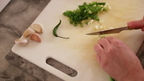 Top-Down-View-Of-Woman-Cutting-Green-Onions-Next-To-Garlic-And-Chili-Pepper-In-Slow-Motion