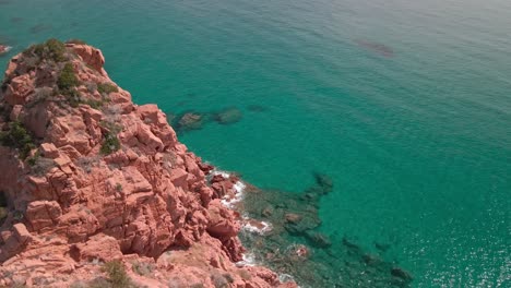 Bird-Eyes-View-Over-a-Red-Cliff-with-Tropical-Water-Sea-on-the-Beautiful-Sunny-Day-In-Sardinia,-Italy---aerial-drone-shot