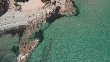 Malerischer-Blick-Auf-Die-Wellen-Des-Tropischen-Und-Kristallklaren-Meeres,-Die-Auf-Die-Felsen-Der-Küste-In-Sardinien,-Italien,-Stürzen---Statische-Drohnenaufnahme-Aus-Der-Luft