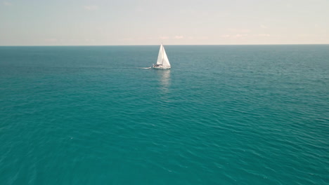 Sailboat-Sailing-The-Blue-Ocean---Beautiful-Calm-Clear-Blue-Sea-During-Summer-In-Sardinia,-Italy---aerial-drone-shot
