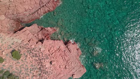 Beautiful-waves-and-red-rock-cliff-of-Sardinia,-Italy-on-a-sunny-day--top-view