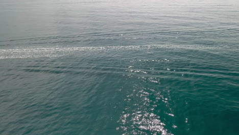 Weißer-Pfad-Und-Kleine-Wellen-Von-Einem-Boot,-Das-über-Die-Smaragdküste-In-Italien-Fährt---Luft-slowmo