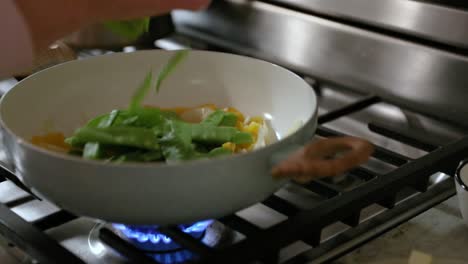 Mujer-Añadiendo-Guisantes-De-Nieve-A-La-Sartén-De-Cocinar-Verduras-En-Cámara-Lenta