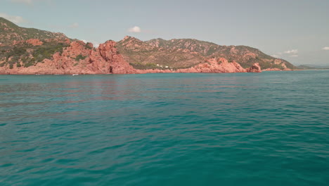 Blick-Auf-Das-Klare-Und-Blaue-Wasser-Der-Smaragdküste-Mit-Den-Roten-Bergen-Im-Hintergrund-Unter-Dem-Sommerferien--Und-Urlaubskonzept-In-Sardinien,-Italien---Luftdrohne