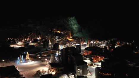 Winter-ski-resort-village-and-hotels-lit-up-at-night,-aerial-view