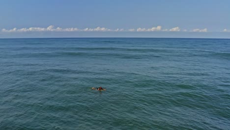 Surfer-paddling-over-waves-in-tropical-water,-aerial-view