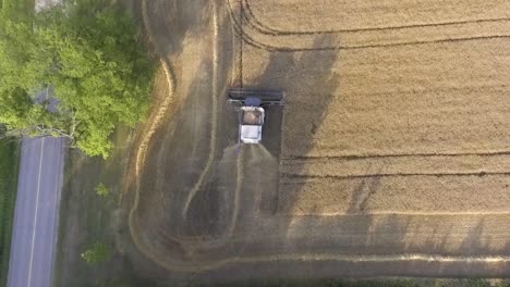 Aerial-View-Flying-Over-Combine-Harvester-Harvesting-Next-To-Rural-Countryside-Road-At-Sunset-In-Slow-Motion