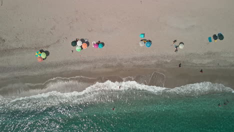 Top-View-Of-Colorful-Umbrellas-At-The-Beach-With-Tourists-Swimming-And-Having-Fun-In-Clear-Blue-Sea