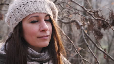 Beautiful-Woman-With-Knitted-Hat-And-Brown-Hair-In-The-Forest-Looks-At-The-Sun-Then-Smiles-At-The-Camera---Slow-Motion,-Close-up