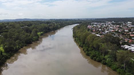 Flying-over-a-brown-river-and-houses-visible-on-the-right