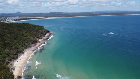 Aerial-view-of-a-peninsula-with-sandy-beach,-rocky-beach-and-surfers-below