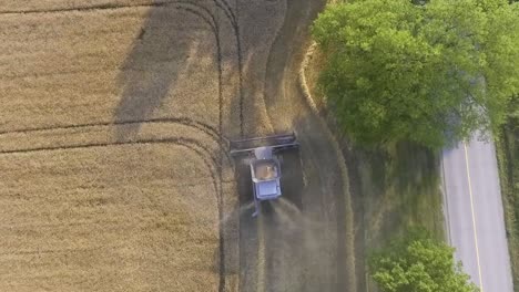 Aerial-View-Flying-Over-Combine-Harvester-Harvesting-Next-To-Rural-Countryside-Road-In-Slow-Motion