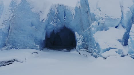 Flying-out-of-glacier-cave-in-snowy-landscape-of-Alaska,-backwards-aerial-shot