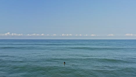Aerial:-surfer-waiting-for-waves-on-surfboard-in-tropical-blue-ocean-water-and-sky