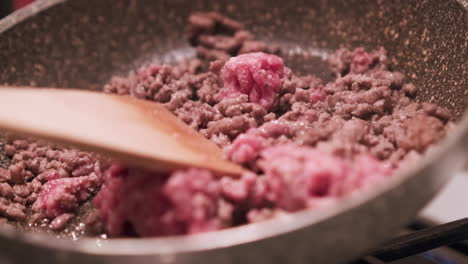 Close-Up-View-Of-A-Wooden-Spoon-Stirring-Raw-Red-Minced-Beef-Meat-In-A-Cooking-Pan-On-Stove-With-Steam---static-shot-in-slow-motion