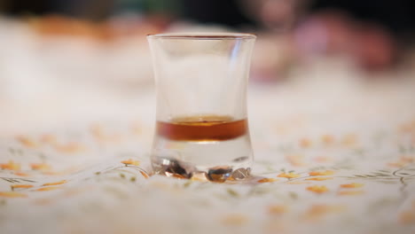 Male-Hand-Puts-Shot-Glass-of-Liqueur-on-Dining-Table,-Close-Up-Selective-Focus