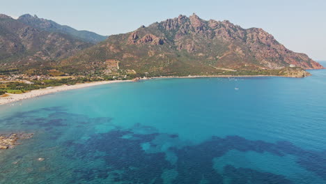 Impresionante-Paisaje-Marítimo-Sardo-Con-Mar-Azul-Claro-Y-Playa-Larga-Con-Montañas-En-El-Fondo-En-Un-Día-Soleado-En-Cerdeña,-Italia---Toma-Aérea-De-Drones