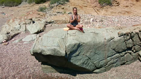 Mujer-Caucásica-Meditando-En-Una-Roca-Junto-A-La-Costa-Del-Mar-En-Cerdeña,-Italia-En-Un-Día-Soleado