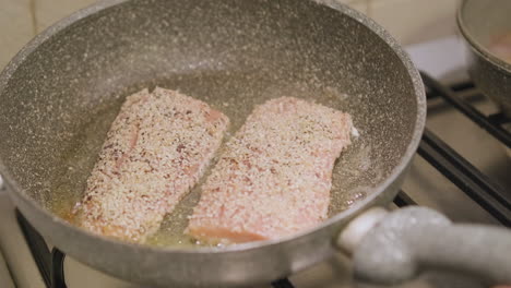 Woman's-Hand-Holding-And-Moving-Pan-With-Delicious-Salmon-Cooking-On-Stove