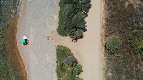 Bird's-Eye-View-Of-Idyllic-Beach-With-Tourists-Under-Umbrella-On-The-Seashore-During-A-Sunny-Warm-Day-In-Sardinia,-Italy---aerial-drone-shot