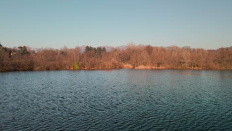 Lago-Ondulado-Con-Vibrantes-árboles-Otoñales-Densos-Contra-El-Cielo-Azul-Al-Atardecer-Durante-El-Invierno-Tardío