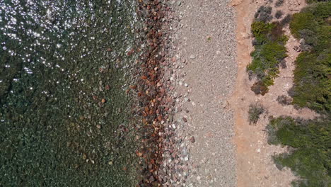 Top-Down-View-Of-The-Transparent-Sea-Waves-Crashing-On-Pebbles-Beach-In-Sardinia,-Italy---aerial-drone-shot