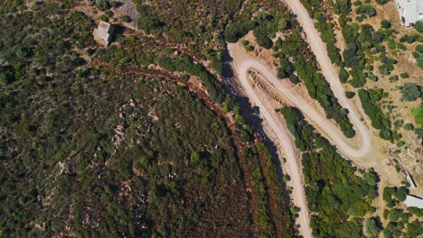 Bird's-Eye-View-Of-The-Dirt-Road-Among-The-Mediterranean-Vegetation-Of-The-Countryside-In-Sardinia,-Italy---Aerial-drone-shot-in-slow-motion