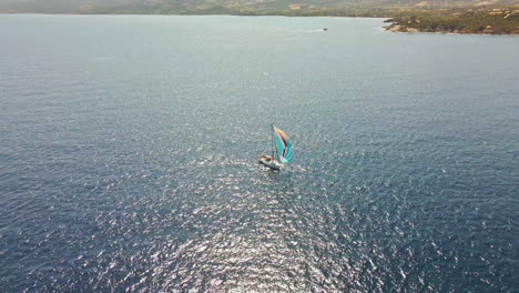 Sailboat-With-Colorful-Sails-Sailing-in-Mediterranean-Sea-by-a-Coast-of-Sardinia-Island,-Italy,-Drone-Aerial-View