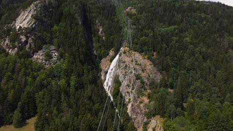 Electric-Cables-Over-The-Alpine-Mountain-With-Green-Forest-And-Waterfall-On-The-Background-In-Italy