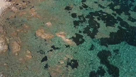 Transparent-Seabed-Under-The-Splendid-Crystalline-Water-Of-The-Sardinian-Sea-With-Small-Waves-Breaking-Against-The-Rocks-In-Sardinia,-Italy---aerial,-top-down
