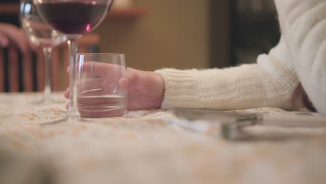 Woman's-Hand-Holding-Glass-With-Water-At-The-Table-During-Family-Lunch-At-Home---close-up,-static-shot