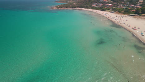 Idyllic-Summer-Beach-With-Colorful-Umbrellas-And-Tourists-On-Vacation-In-Sardinia,-Italy---aerial,-wide-shot