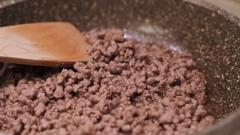 Close-Up-View-Of-Cooked-Minced-Beef-Meat-In-A-Pan-On-Stove-With-Steam-And-Wooden-Spoon-In-Background---slow-motion