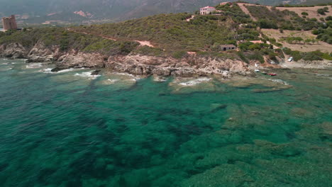 Vista-Panorámica-De-La-Costa-En-El-Mar-Mediterráneo-Azul-Con-Rocas-Y-Vegetación-En-Segundo-Plano-En-Cerdeña,-Italia---órbita-Aérea-De-Drones