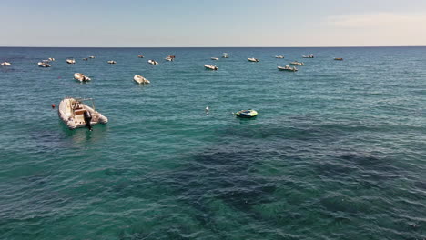 Bergauf-Blick-über-Das-Blaue-Meer-Mit-Einer-Gruppe-Festgemachter-Boote-Mit-Bojen-Vor-Der-Küste-Sardiniens,-Italien---Luftdrohne-Weit-In-Zeitlupe-Gedreht