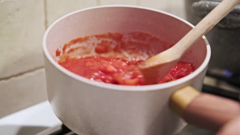 Mixing-Tomato-Sauce-With-Wooden-Spoon-While-It-Cooks-On-The-Stove---close-up,-static-shot