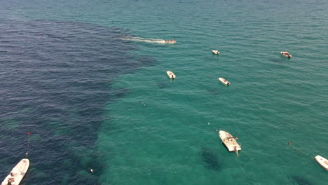 Touristen,-Die-An-Einem-Sonnigen-Tag-In-Sardinien,-Italien,-Mit-Dem-Boot-In-Richtung-Einer-Gruppe-Von-Booten-Im-Meer-Ankommen---Luftdrohne-Weit-Geschossen-In-Zeitlupe