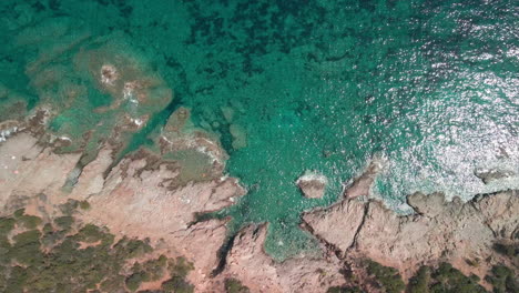 Crystalline-Blue-Sea-With-Waves-Crashing-Against-The-Rocks-Of-The-Mediterranean-Coast-In-Sardinia,-Italy---aerial,-top-down