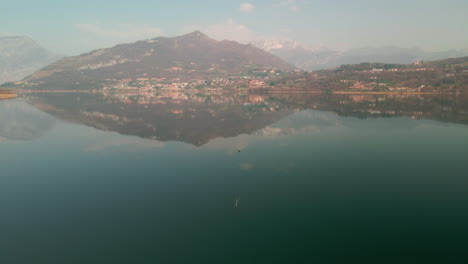 Beautiful-Italian-Landscape-Reflected-On-The-Calm-Water-Of-The-Lake-On-A-Misty-Morning-In-Lago-di-Annone,-Northern-Italy---aerial-drone-shot