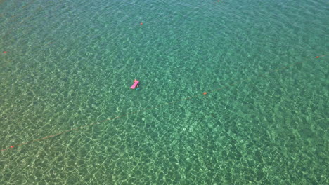 Tourist-With-Airbed-Swimming-In-The-Middle-Of-The-Tropical-Crystal-Clear-Sea-During-Summer-In-Sardinia,-Italy---aerial,-top-down