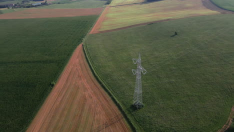 Aerial-View-Of-High-Voltage-Tower-Surrounded-By-Plowed-Fields-Of-Peasants-In-The-Italian-Countryside-During-Sunset-In-Northern-Italy---aerial-drone-shot
