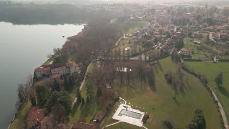 Scenic-View-Of-Residential-Houses-Near-Tranquil-Lake-During-A-Foggy-Afternoon-In-Northern-Italy---aerial-drone-shot