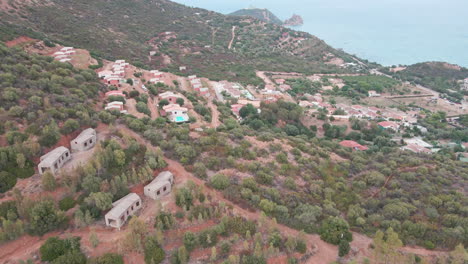 Luftaufnahme-Von-Immobilien-Auf-Einem-Hügel-Der-Insel-Sardinien,-Italien-Mit-Mittelmeerküste-Im-Hintergrund,-Drohnenaufnahme