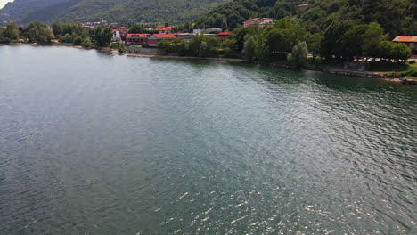 Ruhiges-Wasser-Des-Comer-Sees-Mit-Blick-Auf-Wohnhäuser-Und-Grüne-Vegetation-In-Italien---Drohnenaufnahme-Aus-Der-Luft