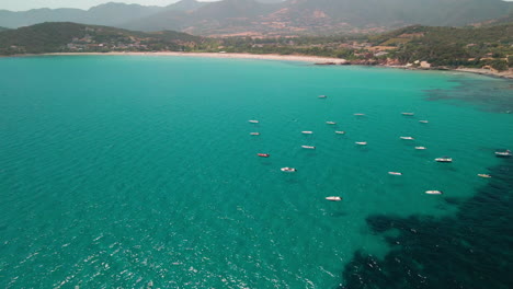 Panorama-Der-Meereslandschaft-Mit-Booten,-Die-Vor-Der-Küste-Unter-Der-Sonne-Und-Der-Berglandschaft-Im-Hintergrund-Auf-Sardinien,-Italien,-Festgemacht-Sind