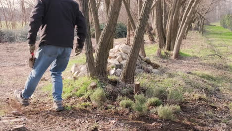 A-Guy-In-Blue-Jeans-And-Black-Winter-Jacket-Walks-And-Cleans-The-Area-in-the-Woods-During-a-Sunny-Afternoon---Static-Shot-in-Slow-Motion