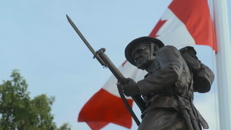 Statue-of-WWI-Canadian-Soldier-statue-with-slow-motion-Canadian-flag-behind,-in-Victoria-BC